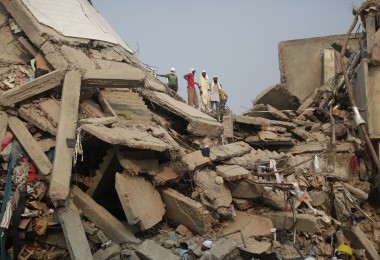 Die eingestürzte Textilfabrik Rana Plaza. Menschen stehen auf den Trümmern.