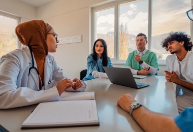 Eine Gruppe aus Männern und Frauen unterschiedlicher Herkunft sitzen an einem Tisch und unterhalten sich.