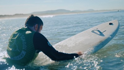 Sicht von schräg hinten: Surfer liegt auf seinem Surfbrett im Wasser.